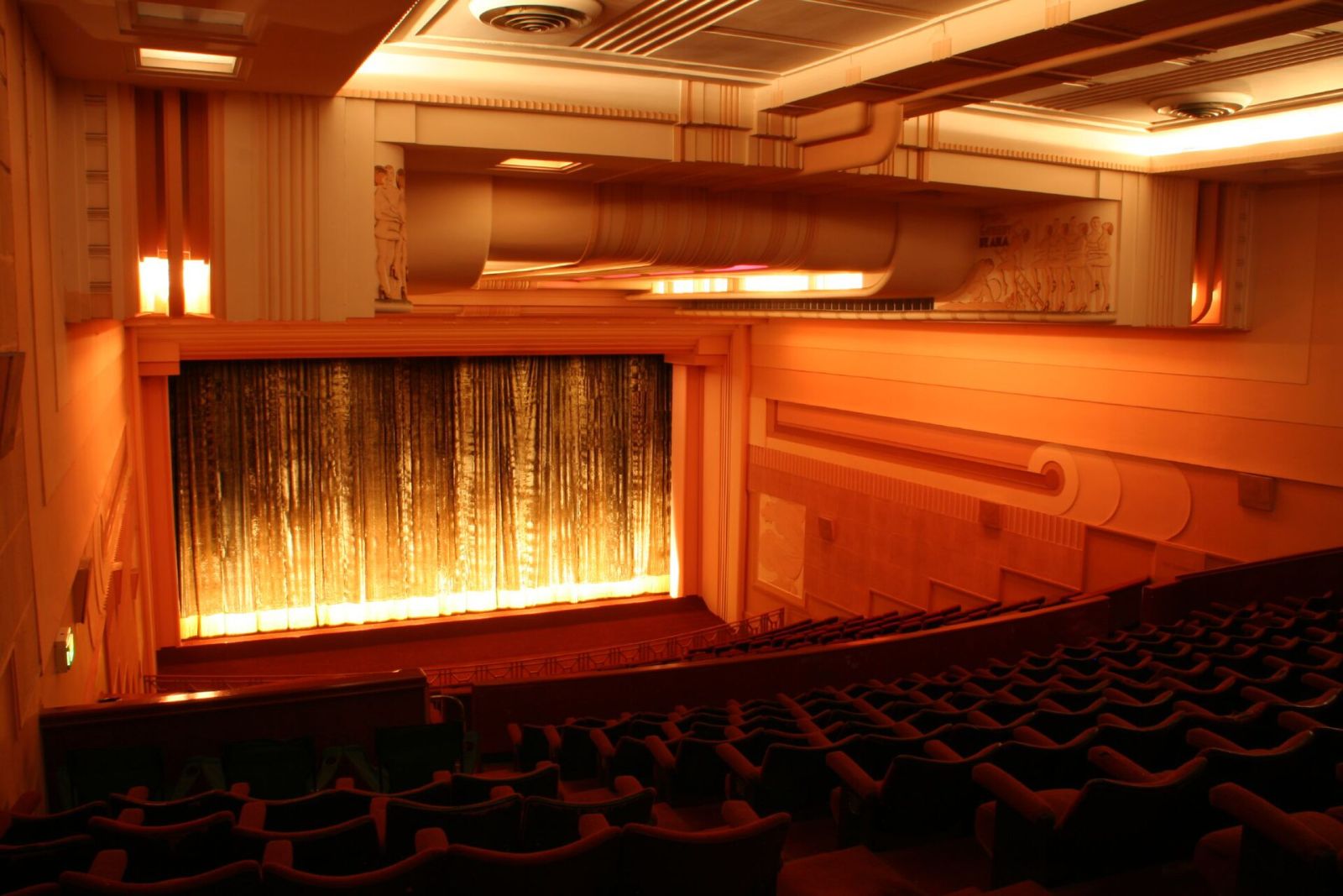 A warm, art-deco cinema hall with a glowing screen and rows of seats
